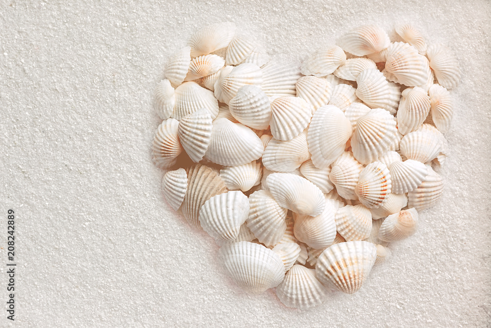  Muscheln liegen in Herzform auf weißem Sand