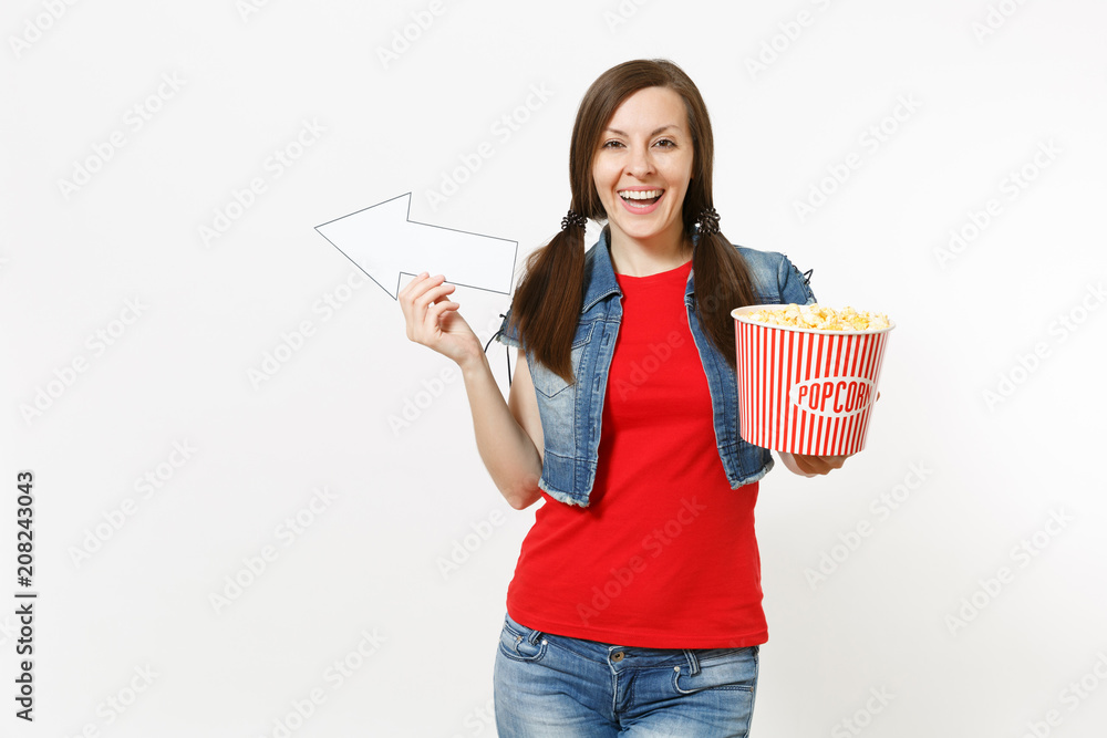 Portrait of young smiling woman in casual clothes watching movie film, holding bucket of popcorn, pointing white arrow aside on copyspace isolated on white background. Emotions in cinema concept. Portrait of young smiling woman in casual clothes watching movie film, holding bucket of popcorn, pointing white arrow aside on copyspace isolated on white background. Emotions in cinema concept.