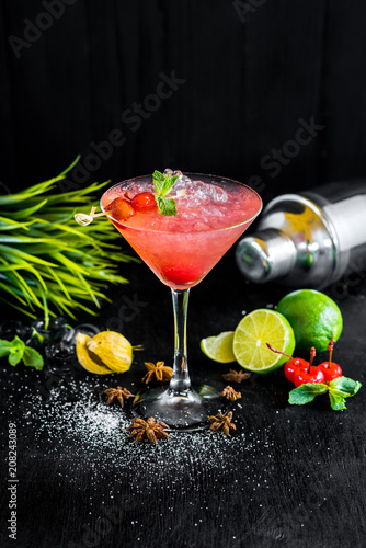 Pink cocktail with cherry and ice on black background