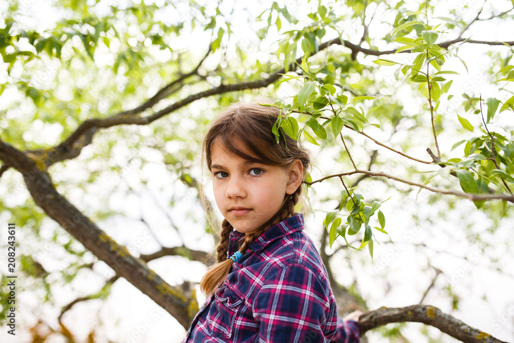 Serious girl with pigtails is standing on a tree branch Serious girl with pigtails is standing on a tree branch