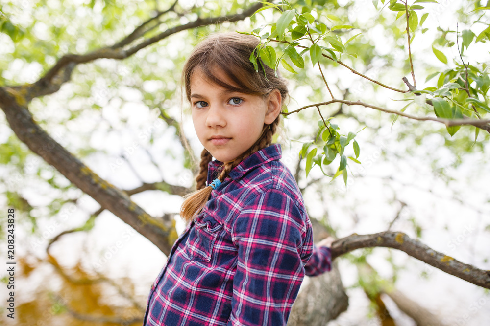 Serious girl with pigtails is standing on a tree branch Serious girl with pigtails is standing on a tree branch