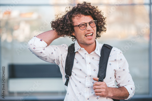 Portrait of unhappy young buasinessman with backpack on the city street. Caucasian male with curly hair, with hand in head, thinking about problem in casual shirt. People and lifestyle concept photo