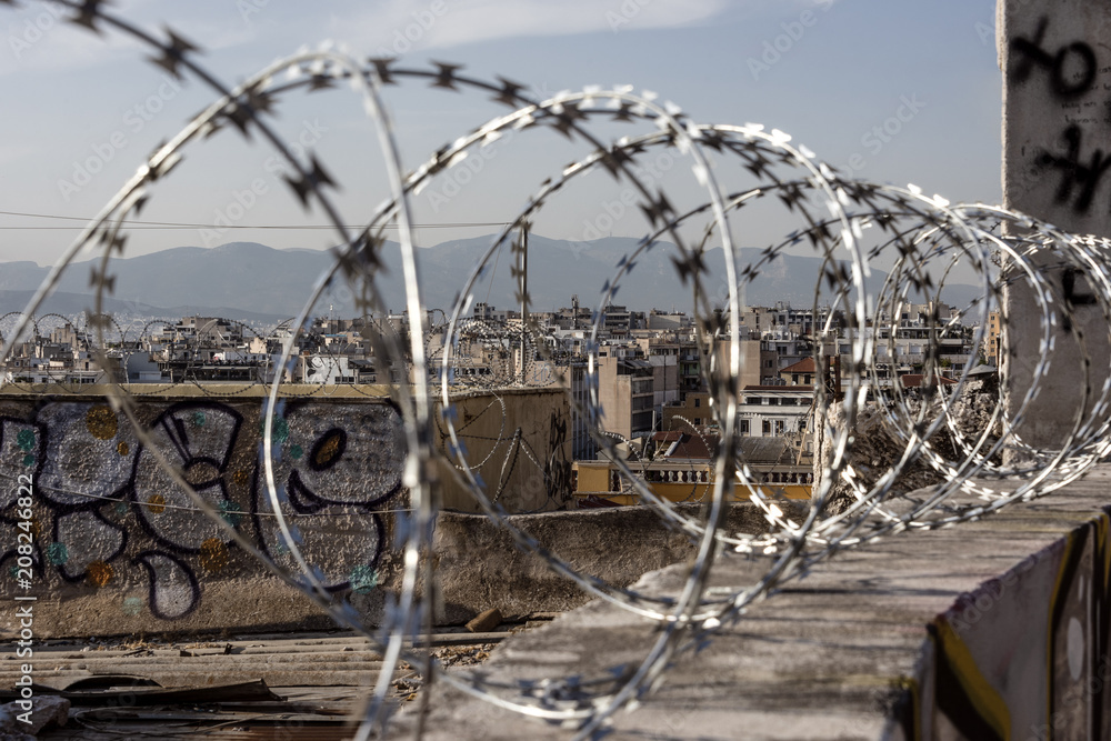 Close up of razor sharp barbed wire with blurred cityscape, skyline, mountain chain and sky in the background - concept security safety crime theft thiefs army military police wired home