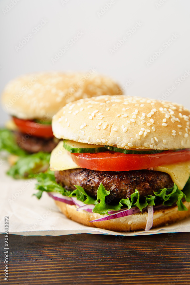 Classical burger with grilled meat, tomatoes, cheese, onion, cucumber and lettuce served on wooden table Classical burger with grilled meat, tomatoes, cheese, onion, cucumber and lettuce served on wooden table
