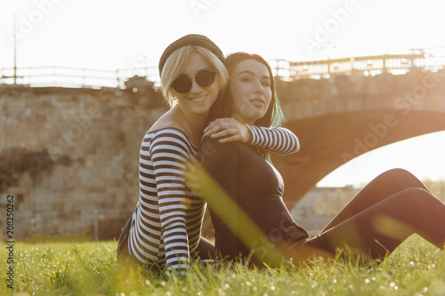 beautiful young women embracing while sitting on grass in park on sunset photo