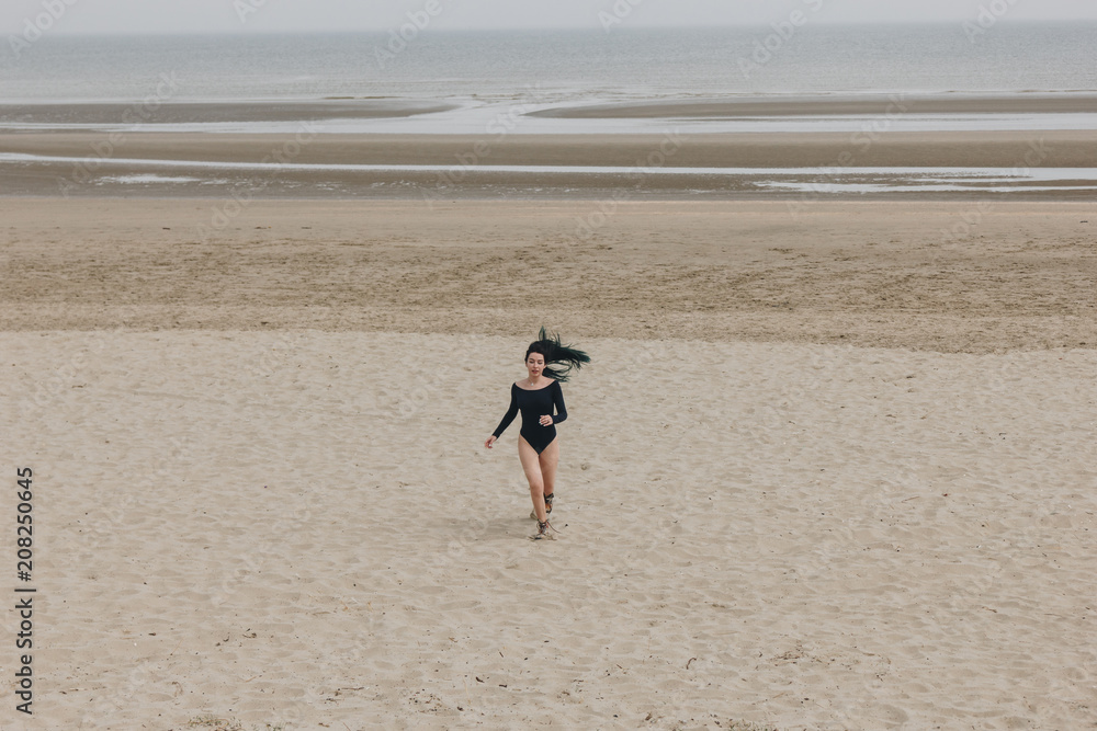 attractive young woman in black bodysuit running on sandy seashore attractive young woman in black bodysuit running on sandy seashore