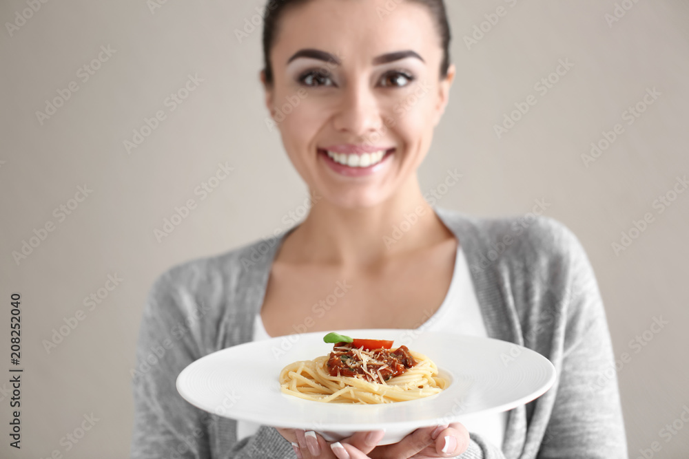 Young woman with plate of tasty pasta on light background
