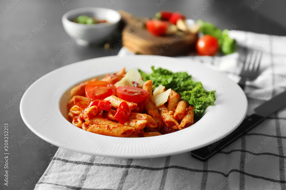 Plate with delicious penne pasta and garnish on table