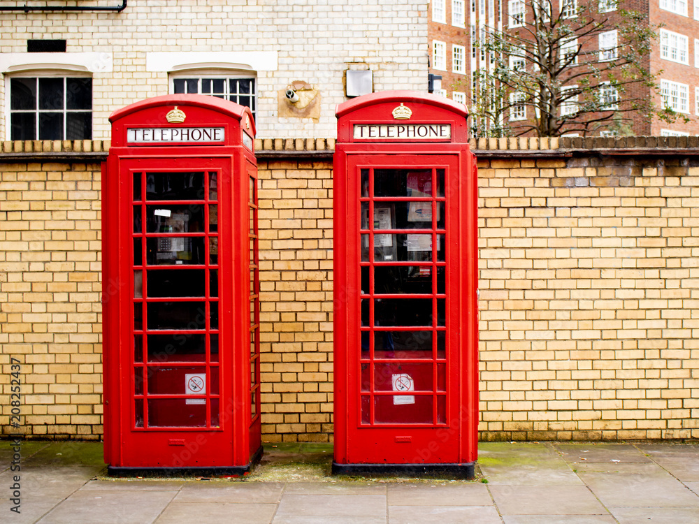 Two Bright Red Traditional British Telephone Boxes in Front of a Brick Wall Two Bright Red Traditional British Telephone Boxes in Front of a Brick Wall