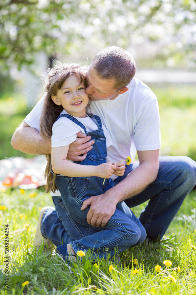 Father hugs his little daughter. Dad and daughter are sitting together in a city park.