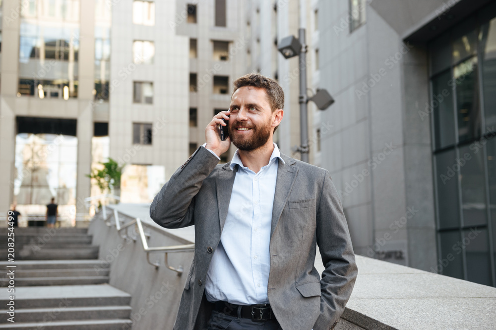 Portrait closeup of smiling joyful business man 40s in gray suit speaking on mobile phone, while walking down stairs outside modern business center Portrait closeup of smiling joyful business man 40s in gray suit speaking on mobile phone, while walking down stairs outside modern business center