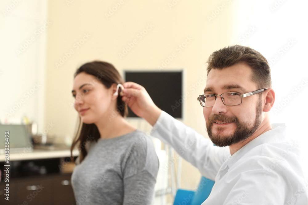 Otolaryngologist putting hearing aid in woman's ear indoors Otolaryngologist putting hearing aid in woman's ear indoors
