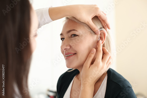 Otolaryngologist putting hearing aid in woman's ear on light background photo