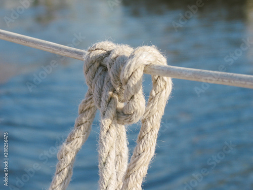 Close-up of 3-strand construction of laid rope forming a clove hitch holding fender in place with a smooth blue-greenish water background bokeh 