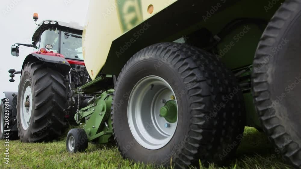 Combine harvester tractor agriculture red metal carriage collects cutted green grass on field, summer cloudy day, close up Combine harvester tractor agriculture red metal carriage collects cutted green grass on field, summer cloudy day, close up