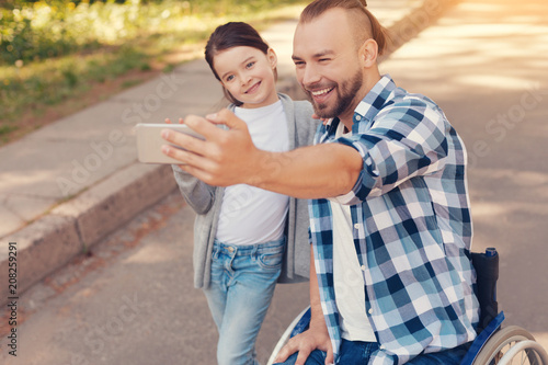Happy moments. Cheerful positive happy man holding a smartphone and smiling while taking a selfie with his daughter