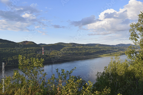 View of the river, wooded hills and wires over the river.