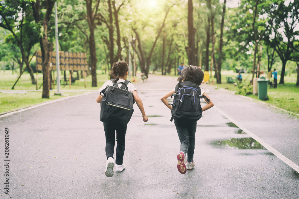 Two pupils of primary school run go to shool. Two girl with bags behind the back. Warm day of fall. Back to school. Little first graders.. Two pupils of primary school run go to shool. Two girl with bags behind the back. Warm day of fall. Back to school. Little first graders..