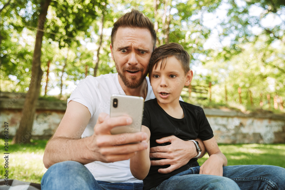 Shocked young father sitting with his little son using mobile phone. Shocked young father sitting with his little son using mobile phone.