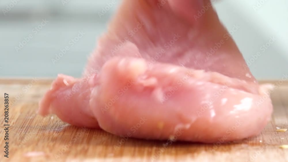 A woman sprinkles seasoning on a chicken breast - closeup A woman sprinkles seasoning on a chicken breast - closeup