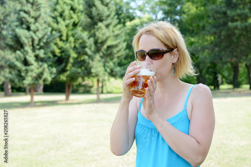 Portrait of happy woman holding glass of beer outside on sunny day.