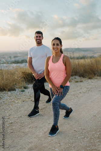 Young couple of athletes stretching legs or doing lunges exercises  for warming up before outdoor running workout.