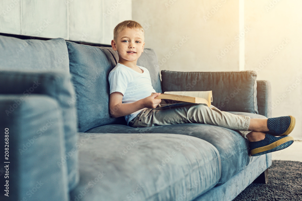 Interesting book. Clever little boy sitting comfortably on his sofa and reading an old book Interesting book. Clever little boy sitting comfortably on his sofa and reading an old book