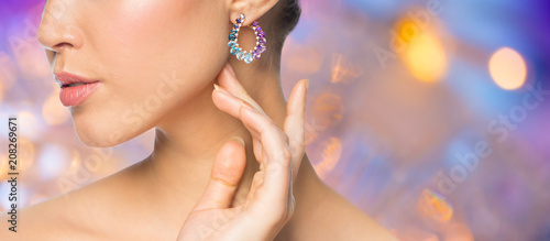 beauty, jewelry and luxury concept - close up of beautiful woman face with earring over holidays lights background