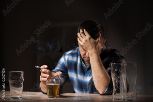 alcoholism, alcohol addiction and people concept - male alcoholic drinking beer and smoking cigarette at night