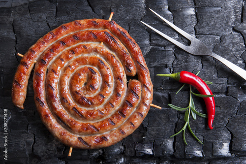 Grilled spiral sausages on a black background of charcoal. 