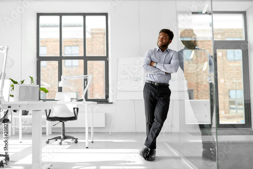 business and people concept - smiling african american businessman at office glass wall