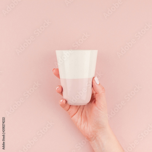 Woman hand holding coffee cup on pink background