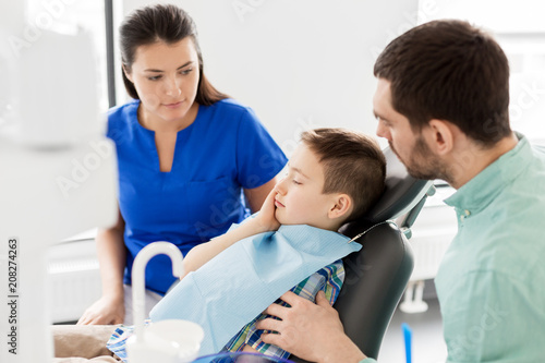 medicine  dentistry and healthcare concept - father and son suffering from toothache visiting dentist at dental clinic