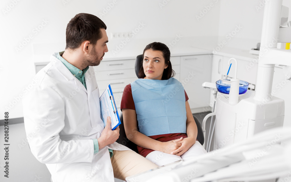 medicine, dentistry and healthcare concept - male dentist with clipboard talking to female patient and discussing teeth treatment at dental clinic office medicine, dentistry and healthcare concept - male dentist with clipboard talking to female patient and discussing teeth treatment at dental clinic office