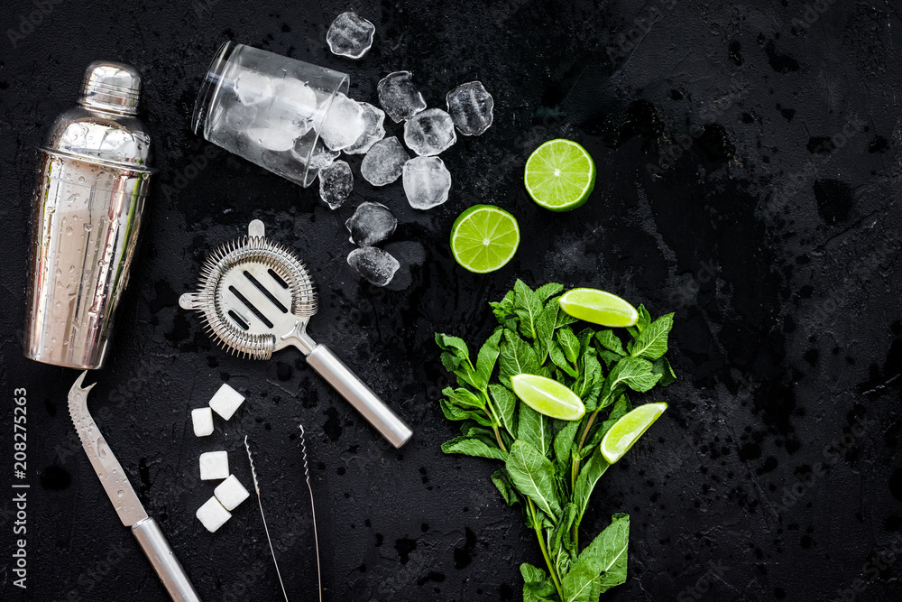 Ingredients and crockery for making mojito. Slices of lime, mint, sugar cubes, glass with ice cubes, shaker, strainer on black background top view copy space Ingredients and crockery for making mojito. Slices of lime, mint, sugar cubes, glass with ice cubes, shaker, strainer on black background top view copy space