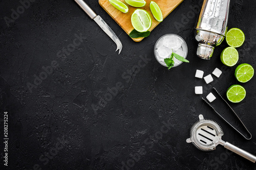 Make mojito cocktail with lime and mint. Shaker, strainer, glass near slices of lime on cutting board on black background top view copy space