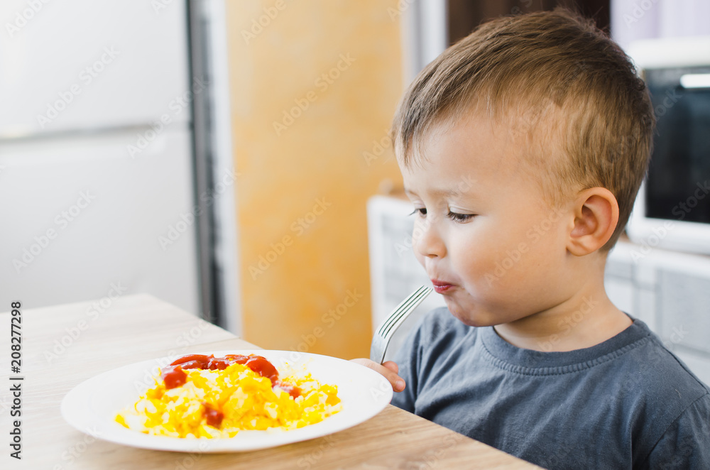 a child in a t-shirt in the kitchen eating an omelet, a fork