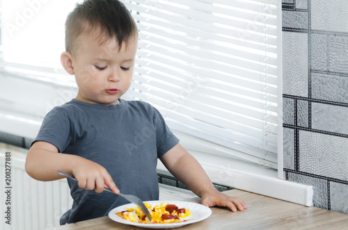 a child in a t-shirt in the kitchen eating an omelet  a fork