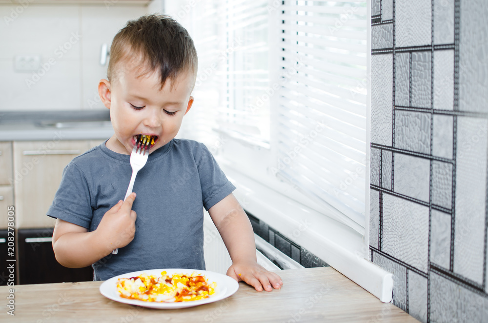 a child in a t-shirt in the kitchen eating an omelet, a fork a child in a t-shirt in the kitchen eating an omelet, a fork
