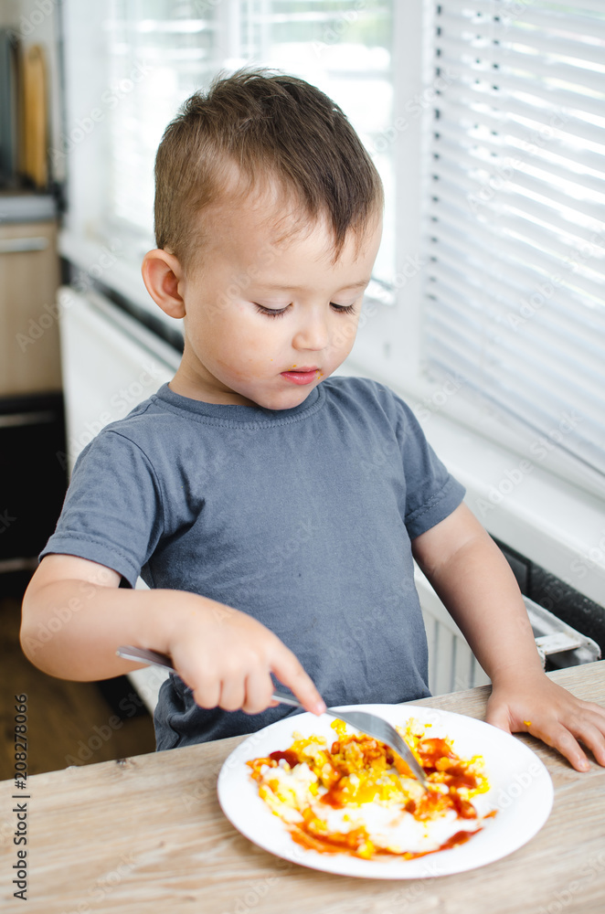 a child in a t-shirt in the kitchen eating an omelet, a fork a child in a t-shirt in the kitchen eating an omelet, a fork