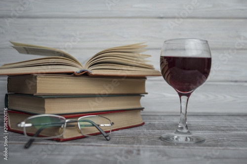 stacked books with glass of wine on a wooden background. Reading Glasses