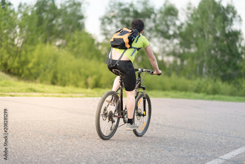 back view of a man with a bicycle and backpack against trees and sky