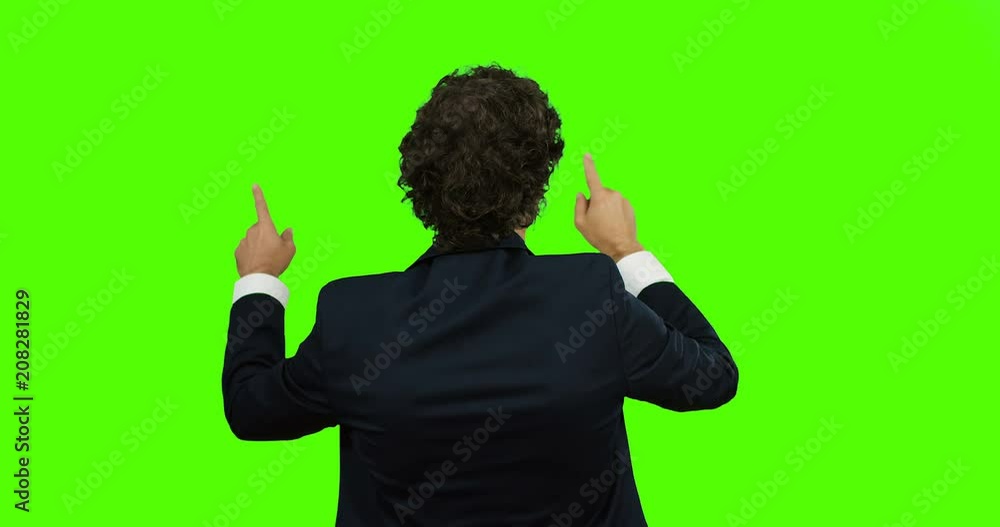 Rear of the Caucasian man in the suit standing back to the camera, scrolling and taping in the air on the Chroma key. Green screen Rear of the Caucasian man in the suit standing back to the camera, scrolling and taping in the air on the Chroma key. Green screen