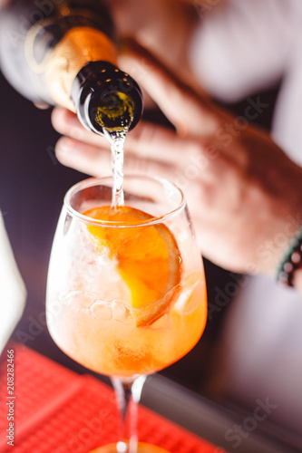 The barman pours champagne into the cocktail of Aperol Spritz close up photo