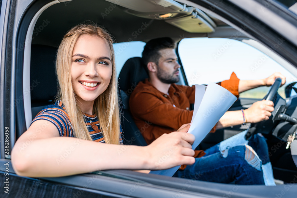 young smiling woman sitting with map in hands while her boyfriend driving car