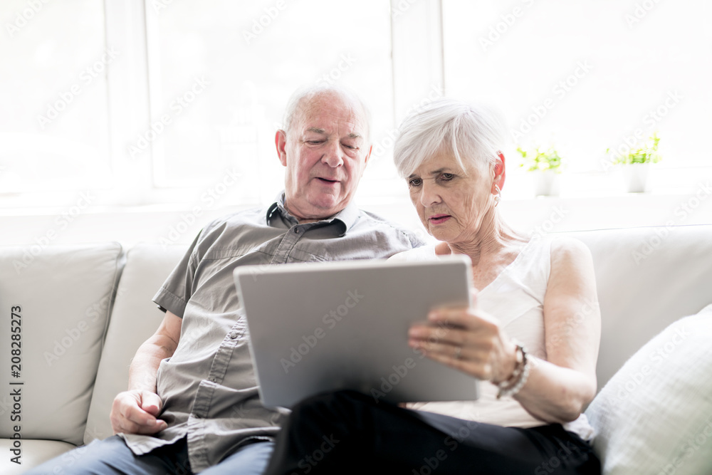 Affectionate attractive elderly couple sitting together on a couch with tablet Affectionate attractive elderly couple sitting together on a couch with tablet