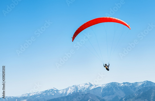 Sportsman on red paraglider soaring over the snowy mountain peaks