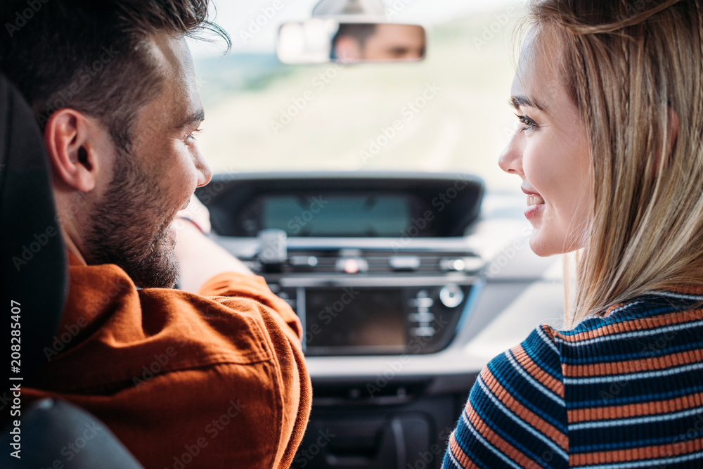 Fototapeta premium side view of smiling couple sitting in car and looking at each other