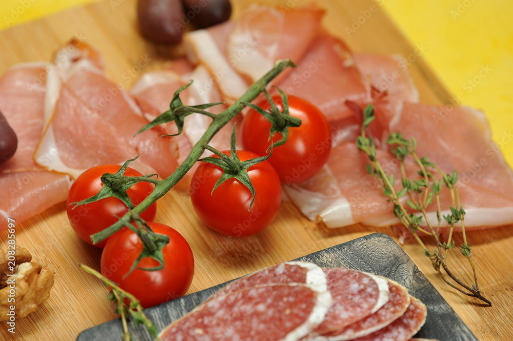 Slices of salami and Parma ham on a wooden board. In the frame, a few cherry tomatoes, a branch of thyme. Close-up. Macro photography. Slices of salami and Parma ham on a wooden board. In the frame, a few cherry tomatoes, a branch of thyme. Close-up. Macro photography.