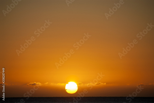 Fototapeta Naklejka Na Ścianę i Meble -  full sun just above horizon at sunrise in middle of low-lying clouds in huge orange sky